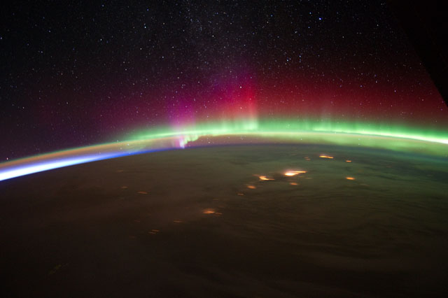 horizon image of earth with lit cities, cloud cover, and bright aurorae